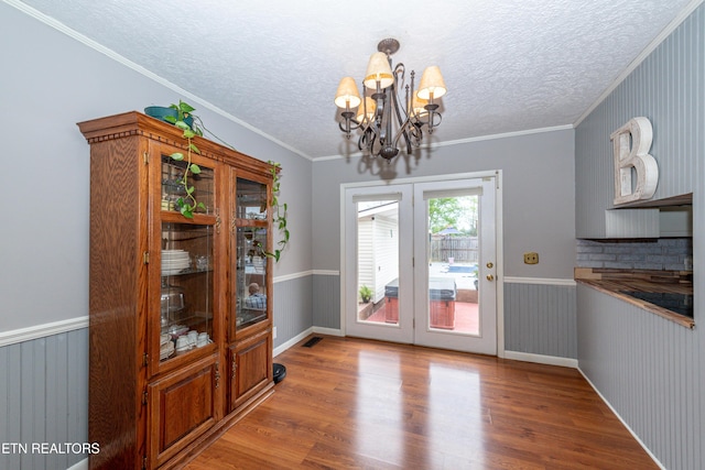 dining space featuring french doors, crown molding, hardwood / wood-style flooring, and a notable chandelier