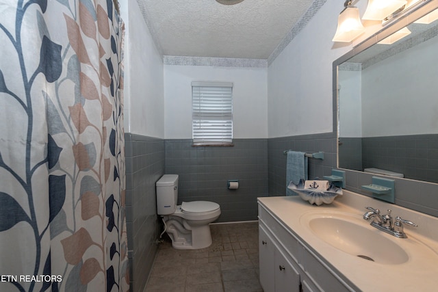 bathroom with toilet, vanity, a shower with curtain, tile walls, and a textured ceiling