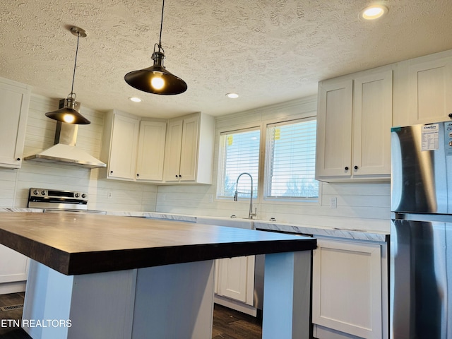 kitchen with wall chimney exhaust hood, stainless steel appliances, butcher block counters, tasteful backsplash, and white cabinetry
