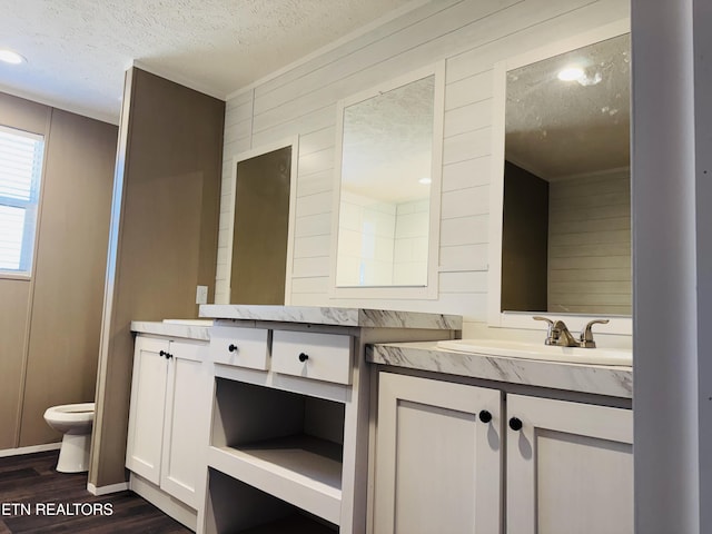 bathroom with toilet, vanity, wood finished floors, wood walls, and a textured ceiling