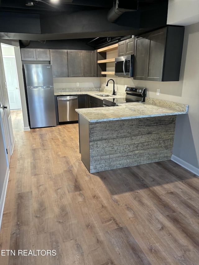 kitchen with light stone countertops, sink, stainless steel appliances, kitchen peninsula, and light wood-type flooring