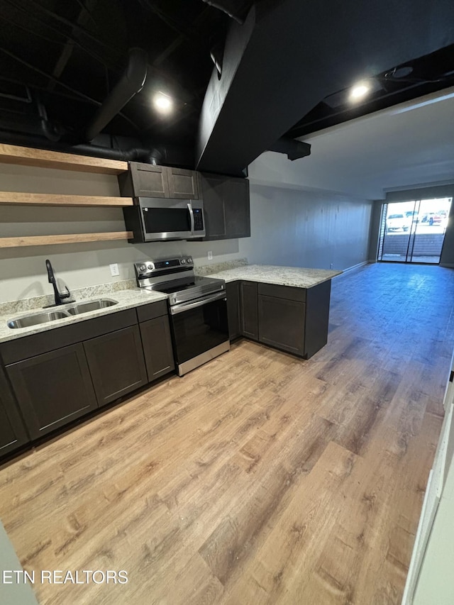 kitchen featuring sink, light stone counters, light hardwood / wood-style flooring, kitchen peninsula, and appliances with stainless steel finishes