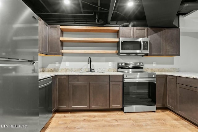 kitchen with open shelves, light wood-style flooring, appliances with stainless steel finishes, a sink, and light stone countertops