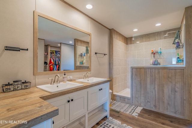 bathroom featuring double vanity, a walk in shower, wood finished floors, and a sink