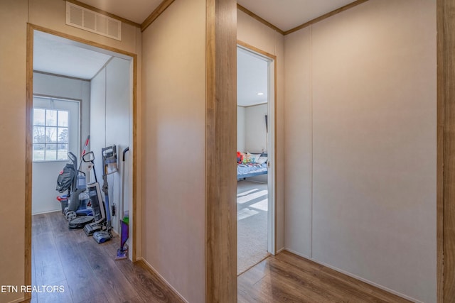 hallway with visible vents, crown molding, and wood finished floors