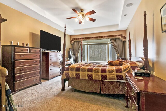 carpeted bedroom with ceiling fan and a tray ceiling