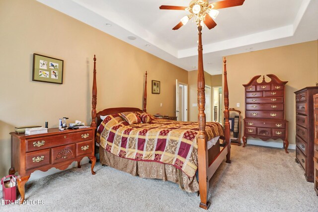 carpeted bedroom with a raised ceiling and ceiling fan