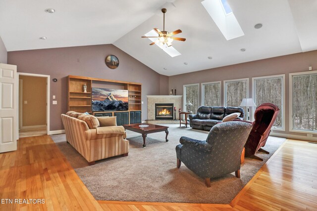 living room with ceiling fan, light hardwood / wood-style floors, and lofted ceiling with skylight