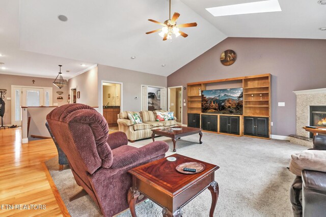 living room with vaulted ceiling with skylight, ceiling fan, and light wood-type flooring