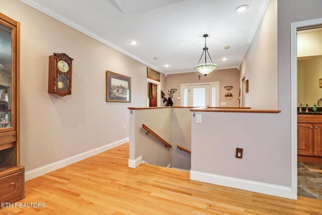 interior space with sink, crown molding, hanging light fixtures, and light hardwood / wood-style flooring