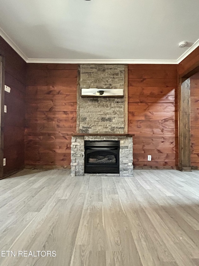 unfurnished living room with light hardwood / wood-style floors, wood walls, ornamental molding, and a fireplace