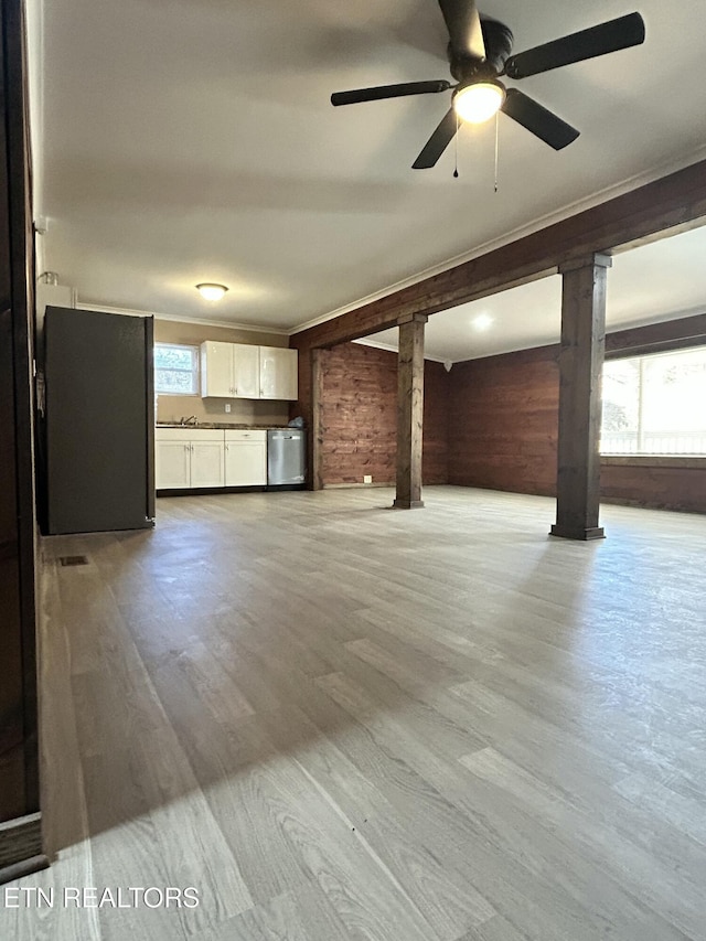 unfurnished living room with wood walls, ceiling fan, a healthy amount of sunlight, and light wood-type flooring