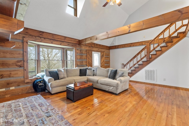 living room featuring ceiling fan, wood walls, lofted ceiling, and light hardwood / wood-style flooring