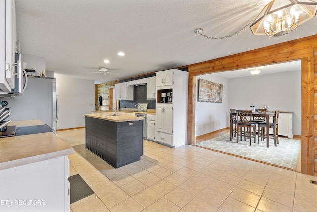 kitchen with backsplash, a kitchen island with sink, white cabinets, ceiling fan with notable chandelier, and hanging light fixtures