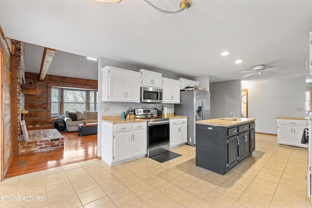 kitchen featuring appliances with stainless steel finishes, ceiling fan, white cabinets, an island with sink, and light tile patterned flooring