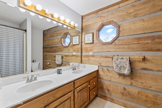 bathroom featuring vanity, wood walls, tile patterned floors, toilet, and a textured ceiling