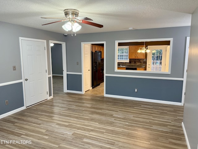 unfurnished living room with wood-type flooring, ceiling fan with notable chandelier, and a textured ceiling