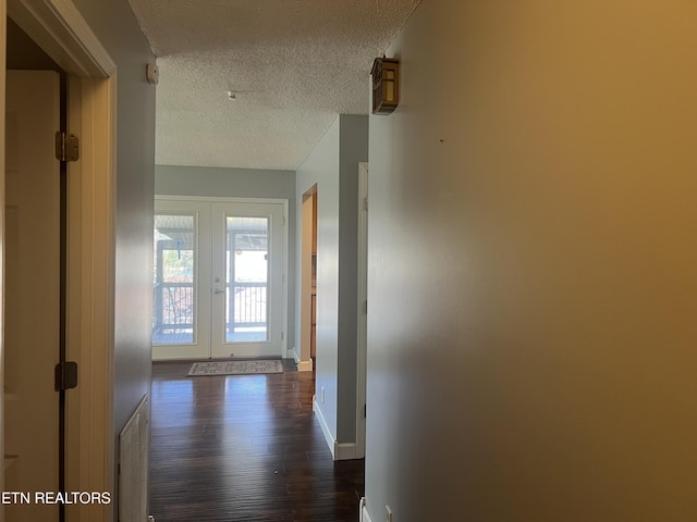 hallway with dark hardwood / wood-style floors, a textured ceiling, and french doors