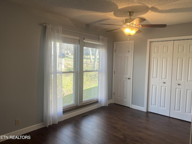 unfurnished bedroom featuring ceiling fan, dark wood-type flooring, a textured ceiling, and multiple windows