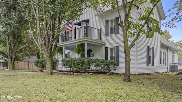 view of front of house featuring central AC unit, a balcony, and a front yard