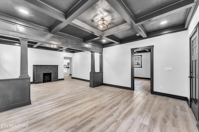 unfurnished living room featuring coffered ceiling, a stone fireplace, light hardwood / wood-style flooring, beam ceiling, and decorative columns