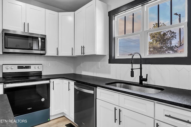 kitchen featuring backsplash, sink, light hardwood / wood-style flooring, white cabinetry, and stainless steel appliances