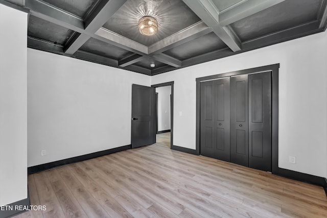 unfurnished bedroom featuring beamed ceiling, a closet, light hardwood / wood-style flooring, and coffered ceiling