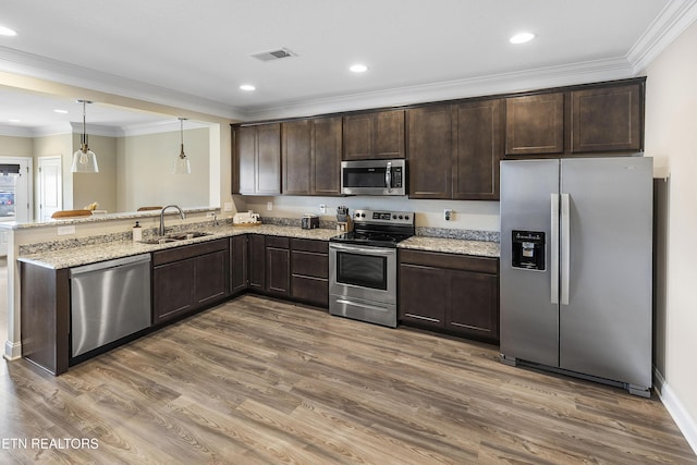 kitchen with light stone counters, stainless steel appliances, sink, pendant lighting, and hardwood / wood-style flooring