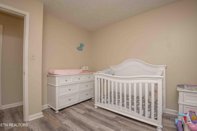 bedroom featuring a nursery area, a textured ceiling, and light wood-type flooring