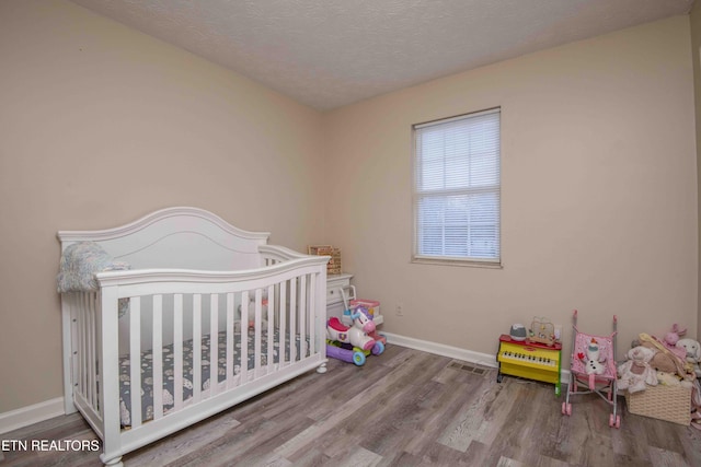 bedroom featuring hardwood / wood-style flooring, a nursery area, and a textured ceiling