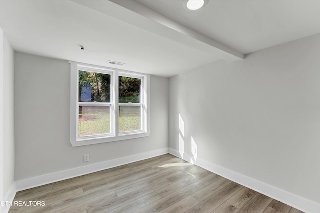 spare room featuring beamed ceiling and light wood-type flooring