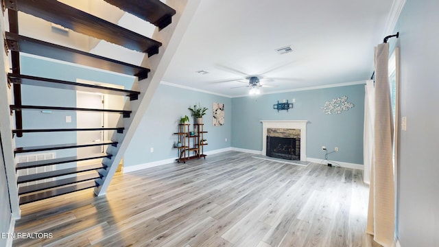 unfurnished living room featuring visible vents, a ceiling fan, ornamental molding, light wood-style floors, and a fireplace