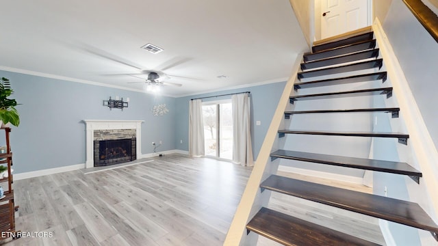 stairs with baseboards, visible vents, wood finished floors, crown molding, and a fireplace