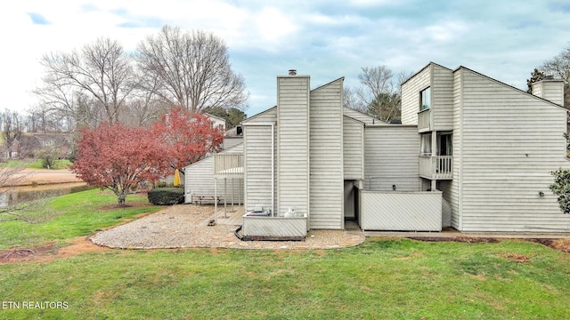 back of house featuring a patio area, a chimney, and a lawn