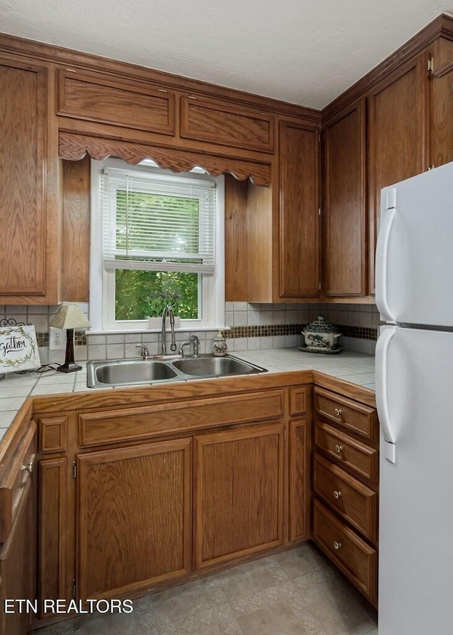 kitchen with white refrigerator, backsplash, tile counters, and sink