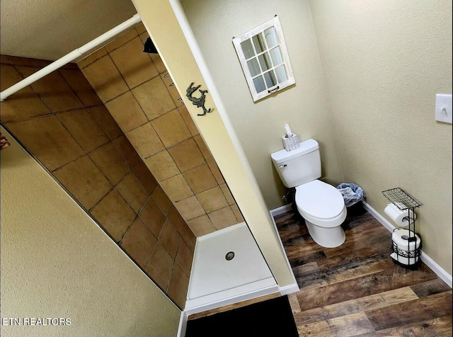 bathroom featuring toilet, a tile shower, and wood-type flooring