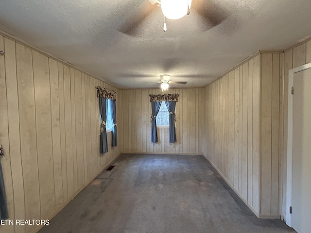 spare room with wood walls, ceiling fan, dark carpet, and a textured ceiling