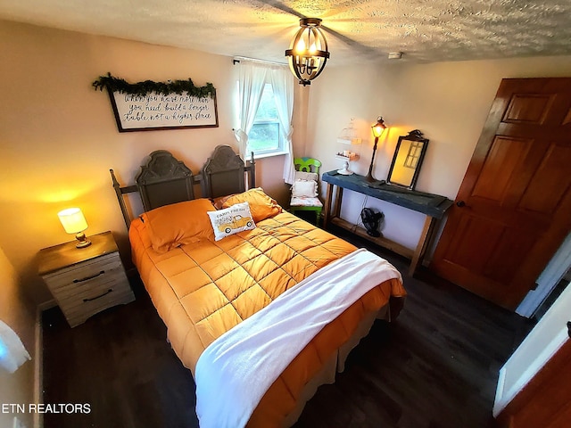 bedroom with a chandelier, a textured ceiling, and dark wood-type flooring