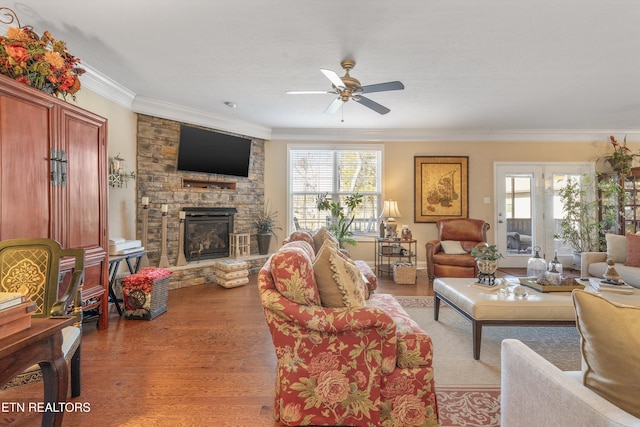 living room featuring ceiling fan, ornamental molding, a stone fireplace, and light hardwood / wood-style flooring