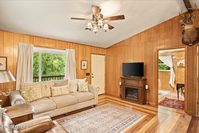 living room with wooden walls, light hardwood / wood-style flooring, ceiling fan, and lofted ceiling