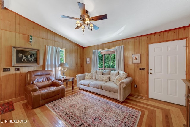 living room featuring ceiling fan, light hardwood / wood-style flooring, wood walls, and vaulted ceiling