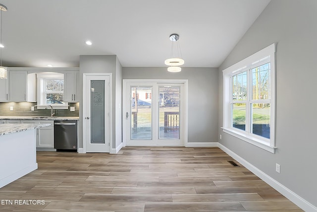 kitchen with pendant lighting, dishwasher, vaulted ceiling, decorative backsplash, and white cabinetry