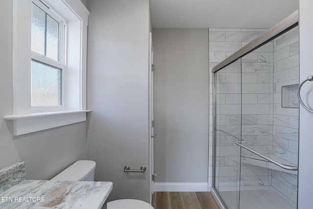 bathroom featuring hardwood / wood-style floors, toilet, a shower with shower door, and a wealth of natural light