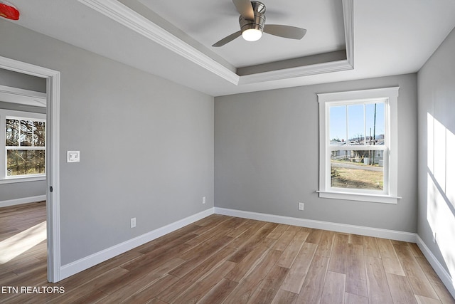 empty room featuring light wood-type flooring, a raised ceiling, and ceiling fan