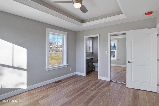 unfurnished bedroom featuring light wood-type flooring, a raised ceiling, ceiling fan, connected bathroom, and a closet