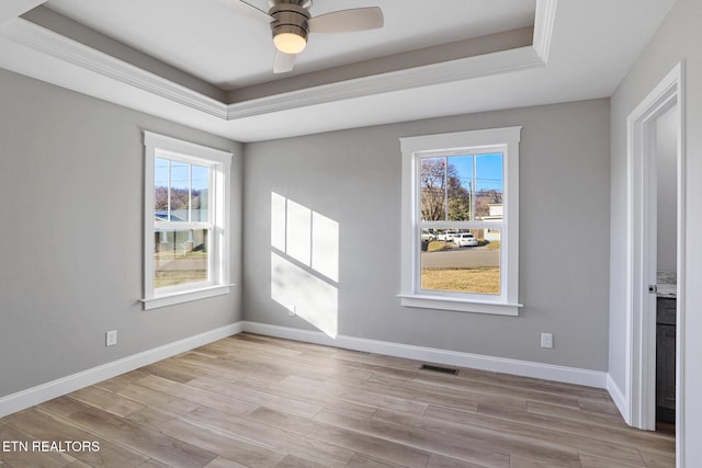 empty room featuring a tray ceiling, ceiling fan, and light hardwood / wood-style flooring