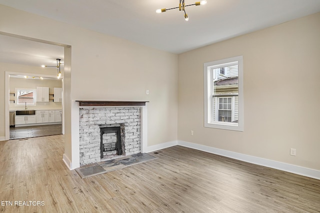 unfurnished living room with a chandelier, light wood-type flooring, a brick fireplace, and sink