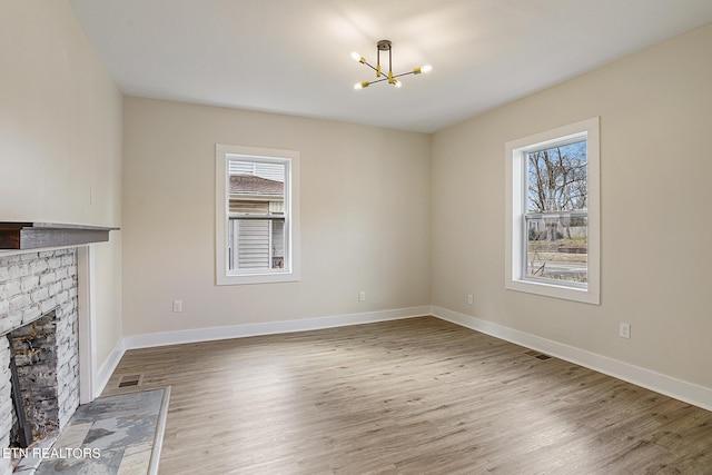 unfurnished living room with a chandelier, wood-type flooring, a healthy amount of sunlight, and a brick fireplace