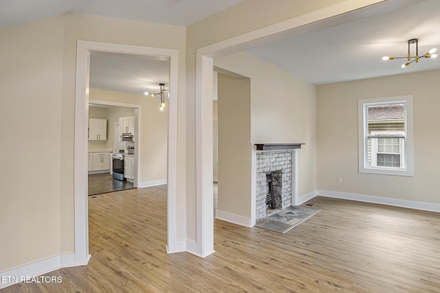 unfurnished living room featuring light hardwood / wood-style floors, a notable chandelier, and a brick fireplace