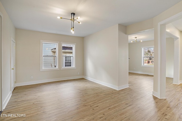 unfurnished room with light hardwood / wood-style floors, plenty of natural light, and a notable chandelier